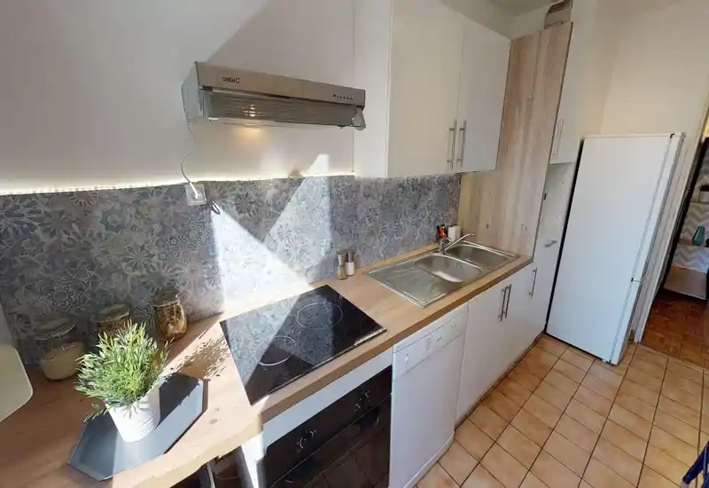 Bright, modern compact kitchen with a ceramic hob, stainless sink, dishwasher and tall fridge. Decorative patterned backsplash and wood-effect countertops create a warm, inviting feel.