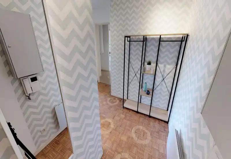 Small entryway with patterned chevron wallpaper, wooden parquet flooring and an open metal shelving unit; bright and tidy space suitable as a hall or foyer.