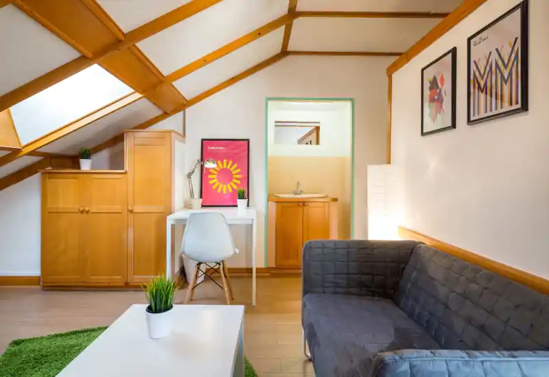 Bright, well-styled attic living area with a comfortable sofa, coffee table and desk beneath a skylight; warm wooden beams and modern décor create a cozy, inviting atmosphere ideal for short-term rentals.