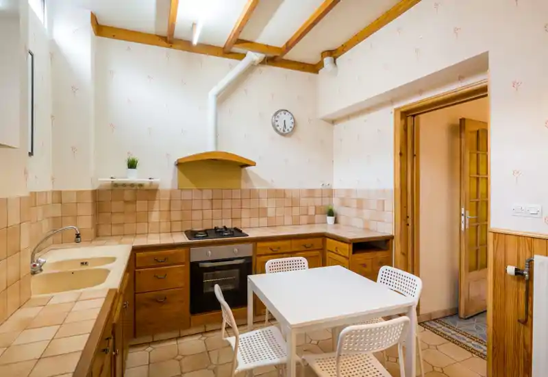 Cucina luminosa e ben tenuta con ante in legno, piani piastrellati e un tavolo da pranzo compatto — ambiente confortevole per pasti informali.