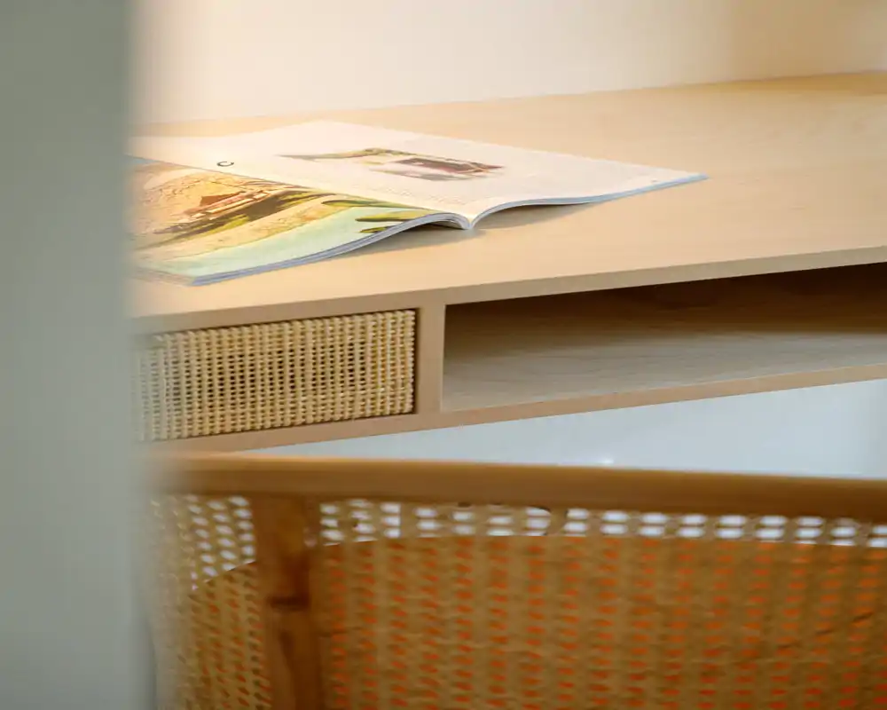 A calm seating corner with a woven-back chair and a light wooden desk surface holding an open magazine — a minimal, warm living area detail.