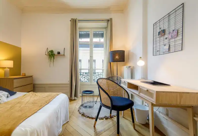 Bright, stylish bedroom with a comfortable bed, warm textiles and a wooden desk by the window — ideal for relaxing or working.