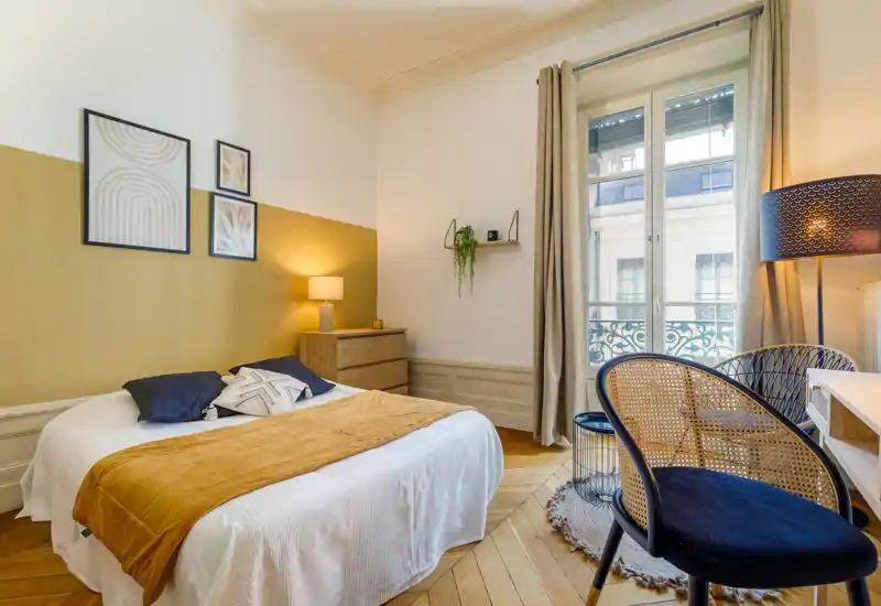 Bright, stylish bedroom with a comfortable double bed, warm textiles and decorative wall art. Large window provides abundant natural light and elegant parquet flooring adds character.