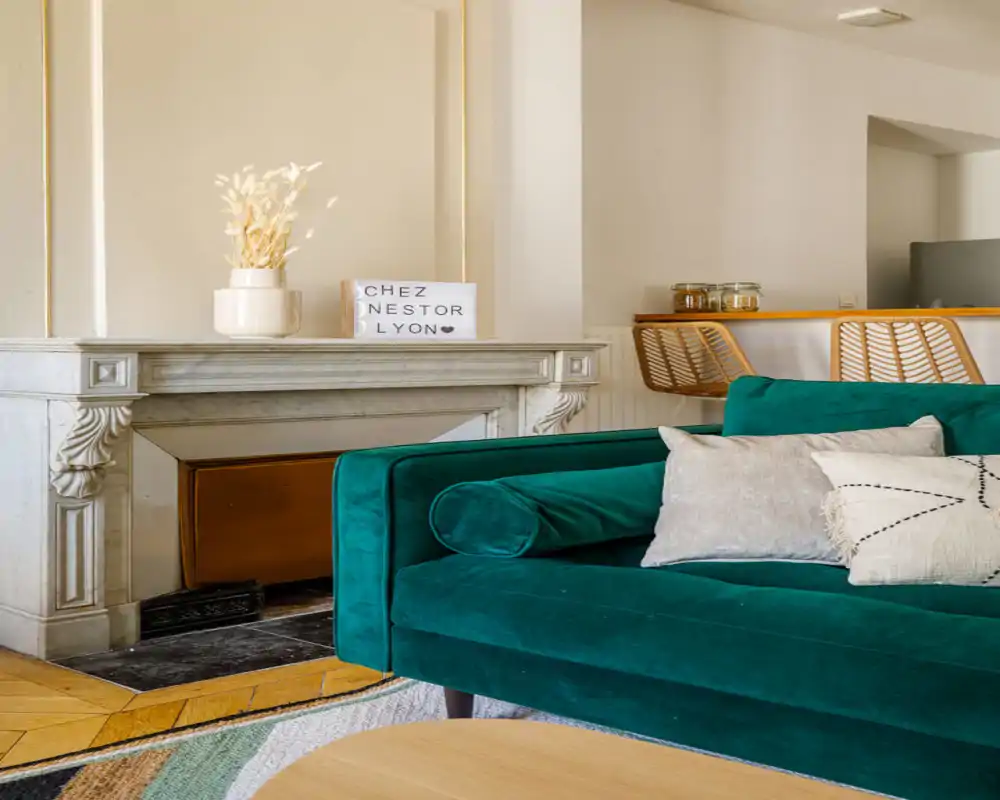 Bright, stylish living area featuring a green velvet sofa, decorative cushions and a classic marble mantelpiece — a cozy, well-styled lounge corner perfect for relaxing.