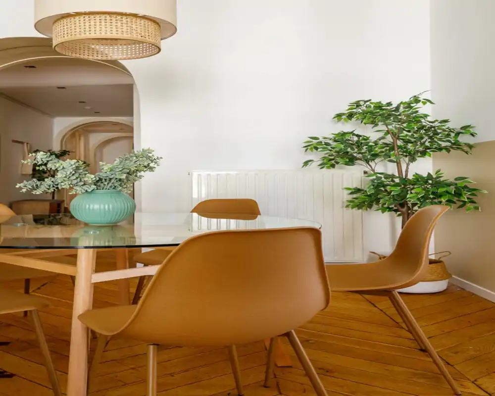 Stylish dining area with a glass-top table, warm-toned chairs, and potted greenery creating a cozy, well-lit atmosphere ideal for meals and small gatherings.