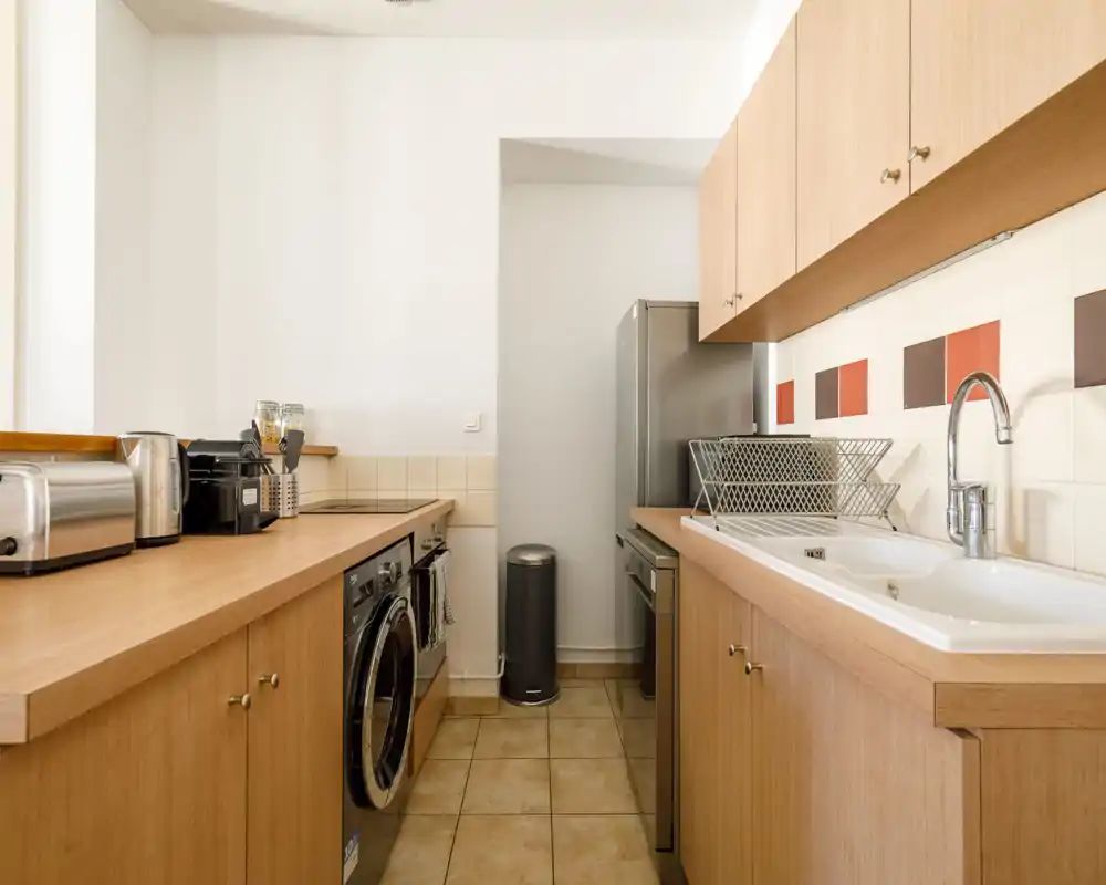 Compact modern kitchen with wood cabinetry, a stainless refrigerator, built-in appliances and a clean sink area — bright, tidy and ideal for short-term rentals.
