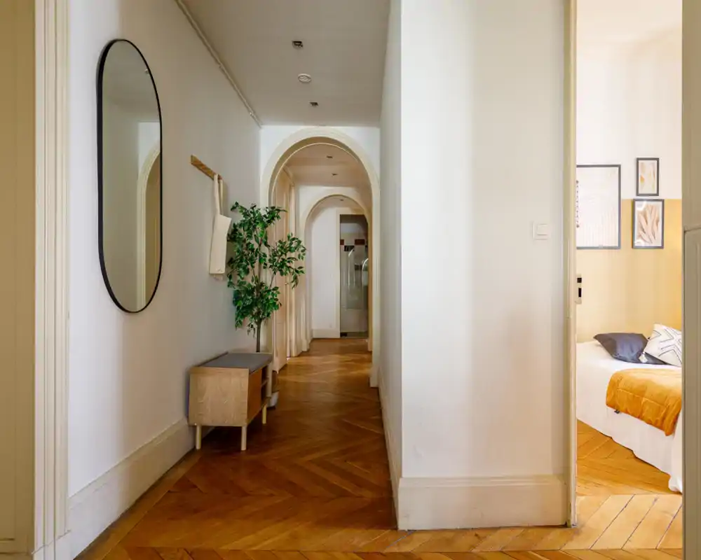 Bright, elegant hallway with warm herringbone wood floors, arched doorways and a minimalist bench with mirror — ideal as an inviting entrance area to the apartment.