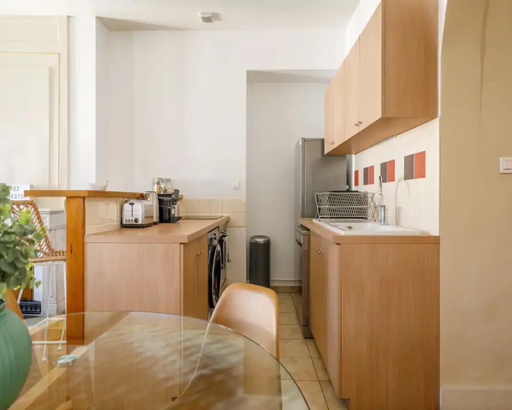 Bright, compact kitchen with wooden cabinets, a sink, stainless appliances and a small breakfast counter—clean, well-styled and ideal for a cozy apartment.