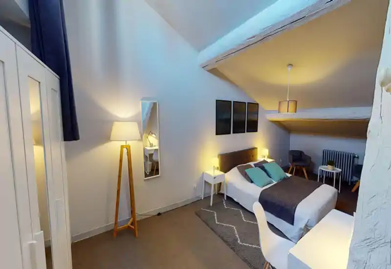 Ampia camera mansardata con letto matrimoniale, comodini e illuminazione calda; cuscini decorativi, tappeto e un angolo salotto rendono l’ambiente accogliente.