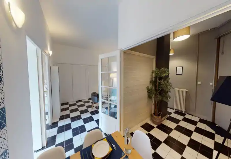 Bright, modern dining area with a set table in the foreground, black-and-white tiled floor and a connected seating/lobby area visible through glass doors.