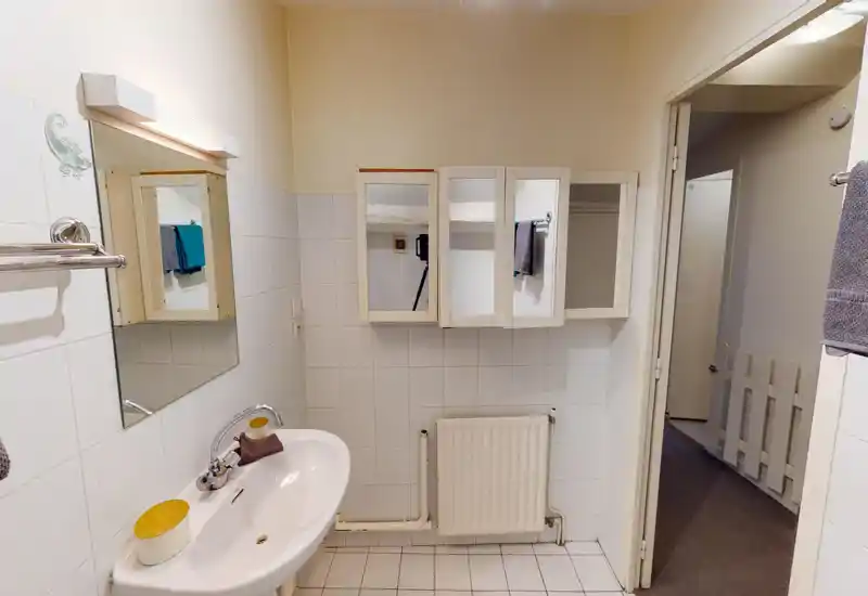 Clean, well-lit bathroom with a wall-mounted mirrored cabinet, sink with faucet, white tiled walls and a radiator under the cabinet.