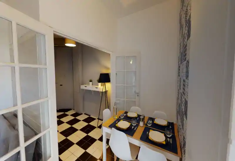 Dining area with a neatly set wooden table for four, modern white chairs and patterned tile accent wall; warm lamp lighting creates a welcoming atmosphere.
