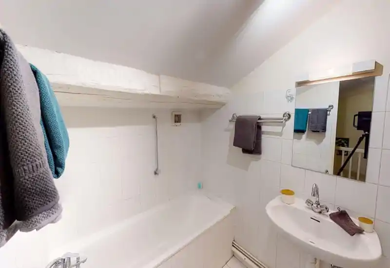 Clean, compact bathroom with a bathtub, pedestal sink, white tiled walls and neatly hung towels; bright, practical space ideal for short stays.