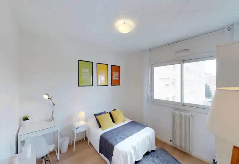 Camera da letto luminosa e moderna con letto matrimoniale ben rifatto, cuscini gialli come accento, una scrivania e una ampia finestra che garantisce molta luce naturale.