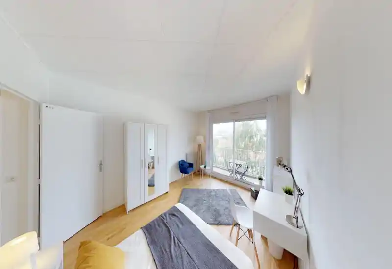 Camera da letto luminosa e moderna con letto in primo piano, armadio bianco, scrivania e un angolo salotto vicino a una grande finestra scorrevole con balcone.
