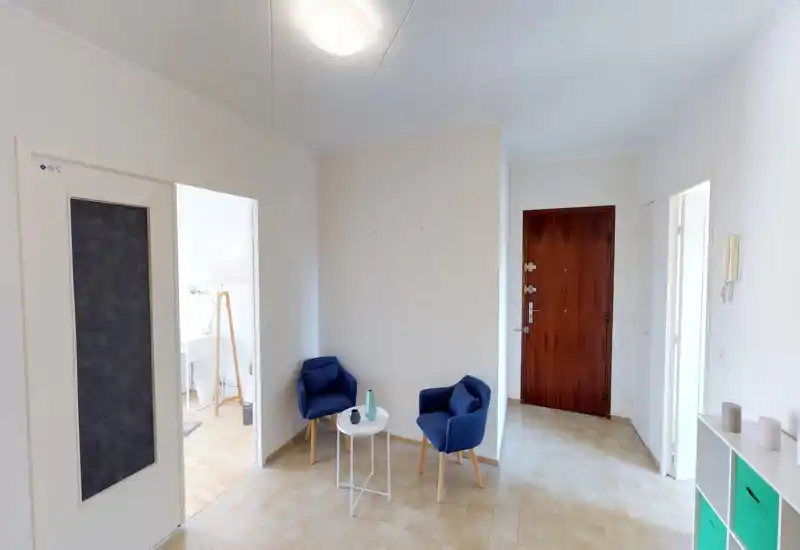 Entrée lumineuse avec porte d'entrée en bois, deux fauteuils bleus et une petite table d'appoint — un hall accueillant au style épuré.