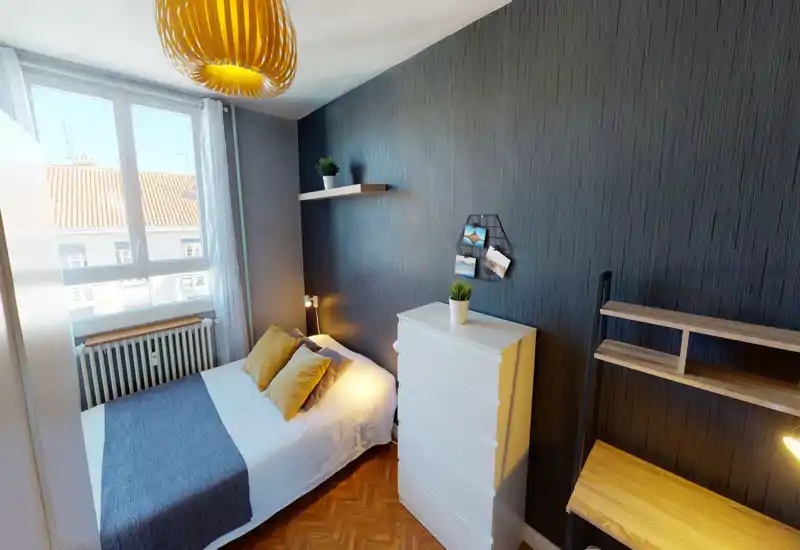 Bright, stylish single bedroom with a comfortable double bed, bedside lamp, white chest of drawers and a work desk; large window provides abundant daylight and warm decorative accents.