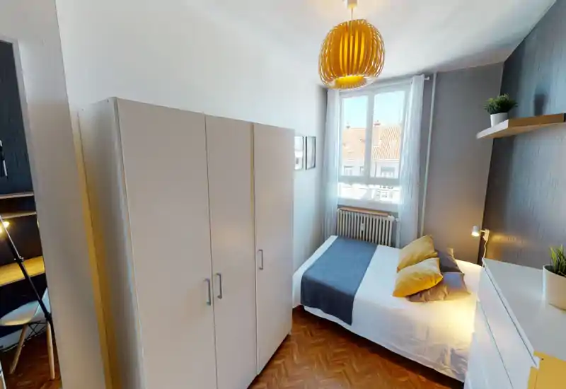 Sunny, well-styled bedroom with a double bed by a window, white wardrobe, wooden parquet and warm accent lighting creating a cozy atmosphere.