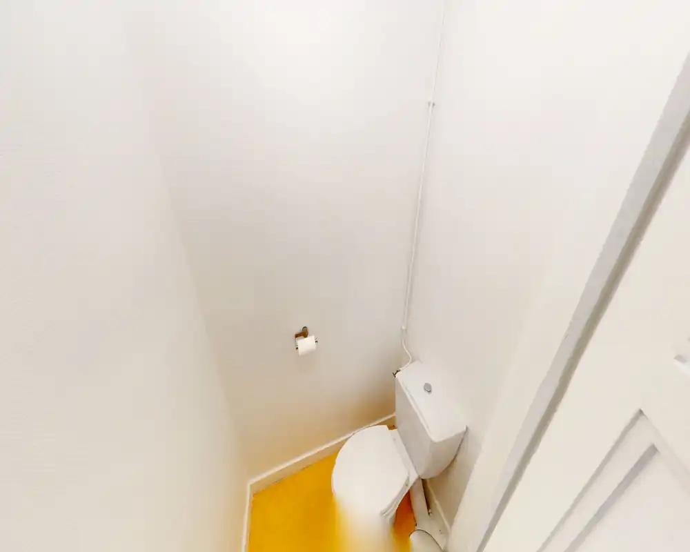 WC compact avec toilette blanche, murs blancs simples et sol jaune chaud ; petit sanitaire propre et bien éclairé.