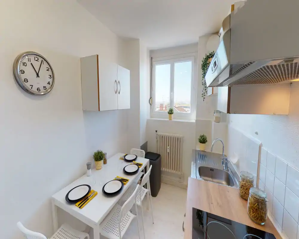 Cuisine compacte et lumineuse avec évier en acier, plaque à induction et petite table dressée pour quatre personnes — idéale pour un appartement urbain.