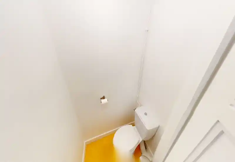 Compact WC with a white toilet, simple white walls and warm yellow flooring; tidy and well-lit small restroom.