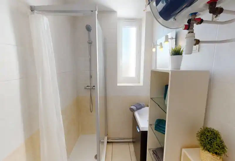 Bright, modern bathroom with a tiled shower area, glass shower screen, compact sink and open shelving with towels and plants.