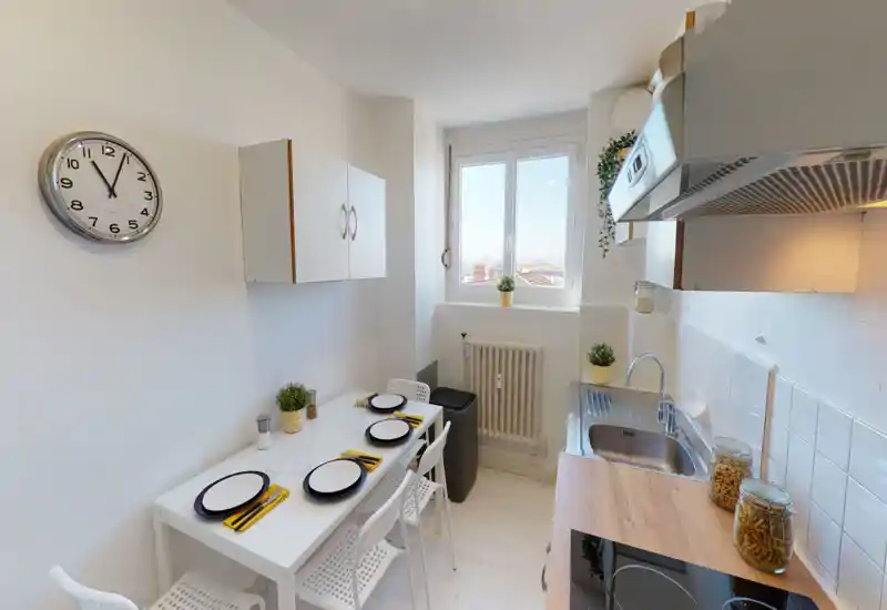 Bright, compact kitchen with a stainless sink, induction hob and a small dining table set for four — ideal for a cozy city apartment.