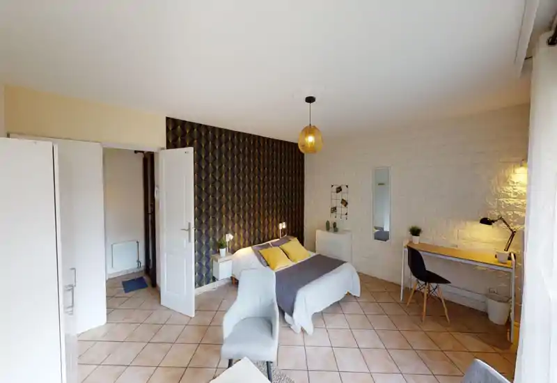 Bright, stylish bedroom with a double bed framed by patterned wallpaper, bedside tables and a study desk by the window — comfortable and well-lit for work or rest.