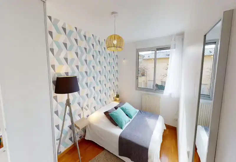 Bright, stylish bedroom with a double bed, decorative geometric wallpaper, bedside lamps and natural light from a window — cozy and well-styled for short-term rentals.