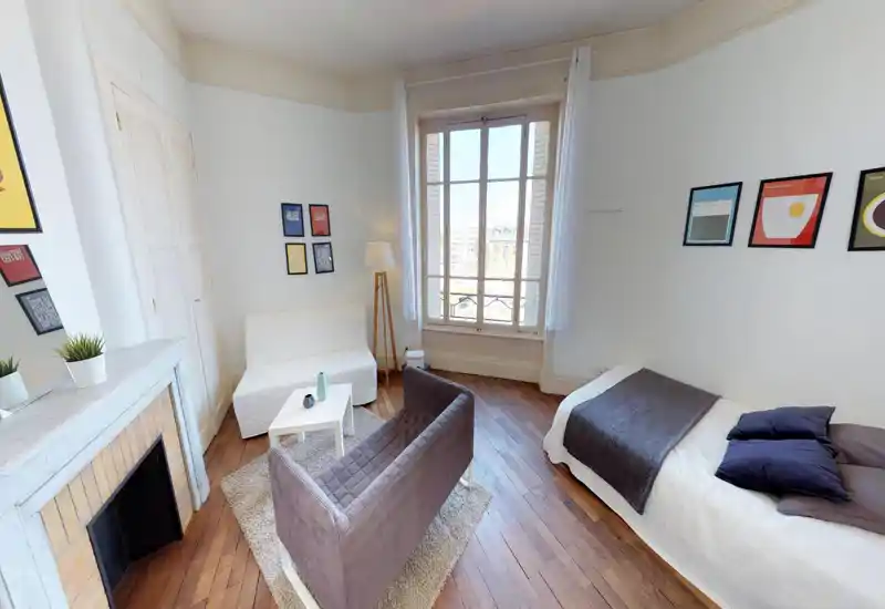 Bright, stylish bedroom with a single bed tucked against the right wall, soft cushions and a gray throw. Wooden parquet, large window with shutters and a cozy seating area make the room inviting for short stays.