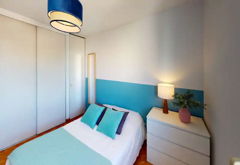 Bright, well-styled bedroom with a double bed dressed in soft aqua textiles, a bedside chest with lamp and plant, and built-in wardrobes for storage.