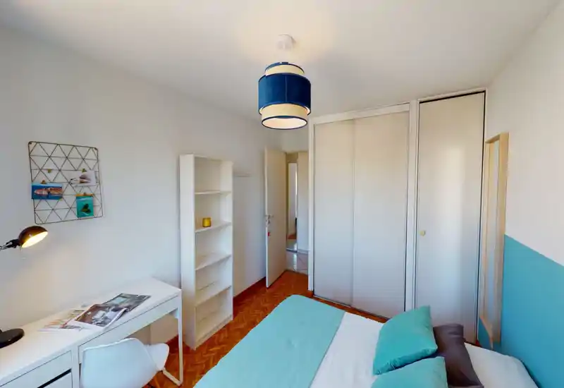 Bright, modern bedroom with a visible double bed dressed in teal linens, a white desk and shelving, and a built-in wardrobe—clean, well-lit space ideal for a rental listing.