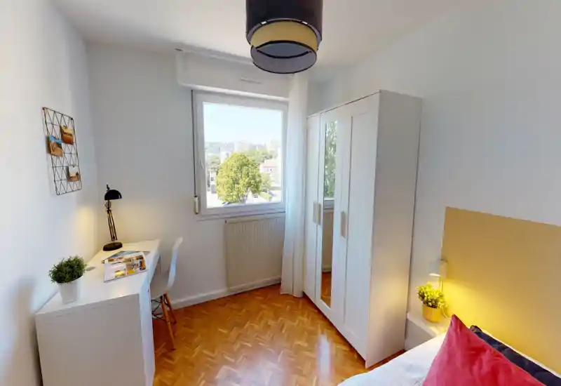 Sunny, tidy bedroom with a comfortable bed, bedside lamp and wardrobe. The room features a study desk by the window and warm wooden flooring, ideal for a quiet, bright stay.