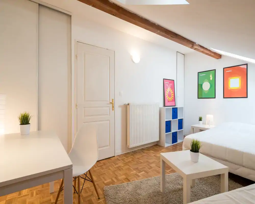 Bright, modern attic bedroom with a large white bed, minimalist furnishings, wooden parquet and decorative framed prints — ideal for a comfortable stay.