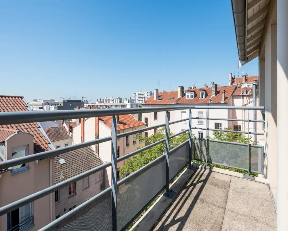 Sunny balcony with metal railing and a view over neighboring rooftops, ideal for morning coffee or relaxing outdoors.