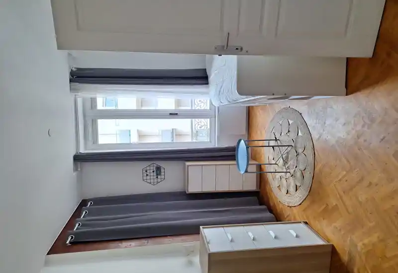 Bright, tidy bedroom with a single bed by the window, wooden parquet floor, neutral curtains and minimalist storage units.