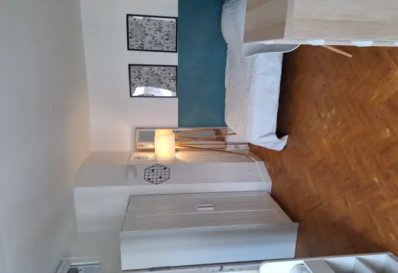 Bright, neatly styled bedroom with a double bed, wooden parquet floor, standing lamp and decorative wall art—ideal for a cozy short-term stay.