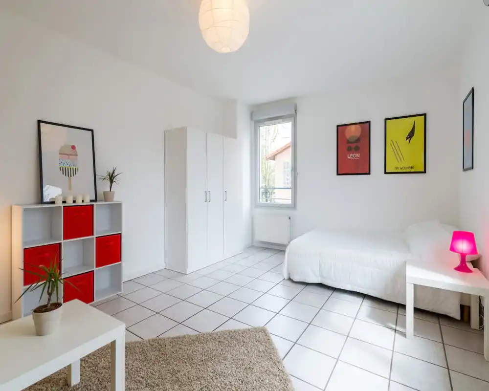 Bright, minimalist bedroom with a double bed, white wardrobe and modern decorative prints. The room features tiled floors, a cozy rug and pops of red and pink for a fresh, contemporary look.