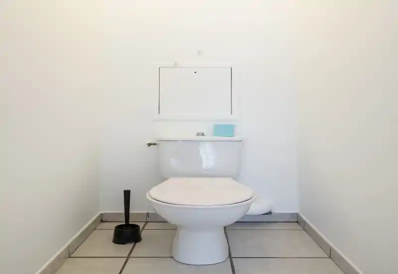 Compact, clean bathroom with a white toilet, tiled floor and a toilet brush — bright, minimal and well-lit.