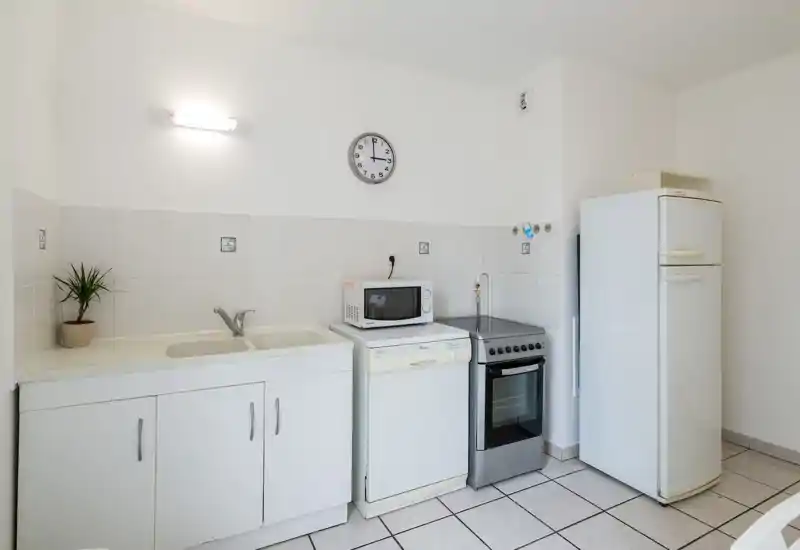 Clean, compact kitchen with a double sink, microwave, dishwasher, freestanding oven and fridge; bright white tiles and simple finishes suitable for short-term rentals.