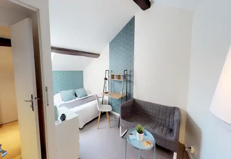 Bright, cozy attic bedroom with a double bed, patterned accent wall, small desk and a compact sofa — ideal for a comfortable short stay.