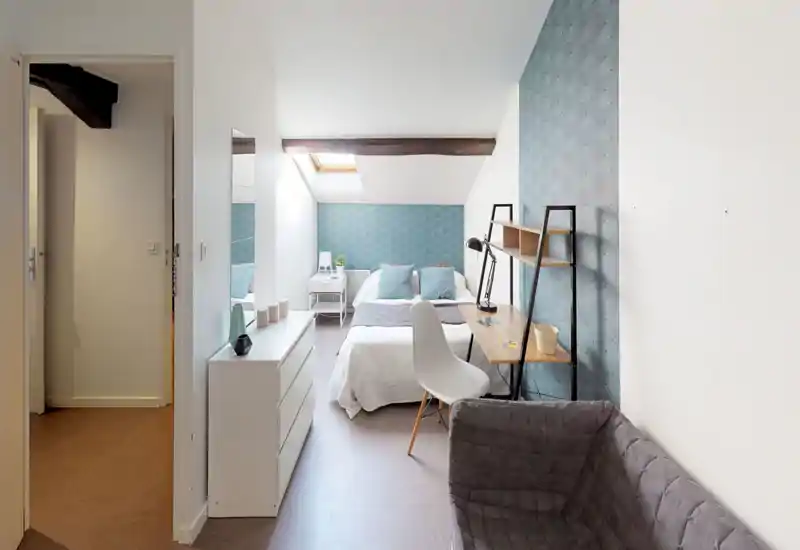 Bright, neatly styled attic bedroom with a double bed under a skylight, coordinating blue patterned wallpaper and a small desk by the bed — ideal for a cozy single or couple.