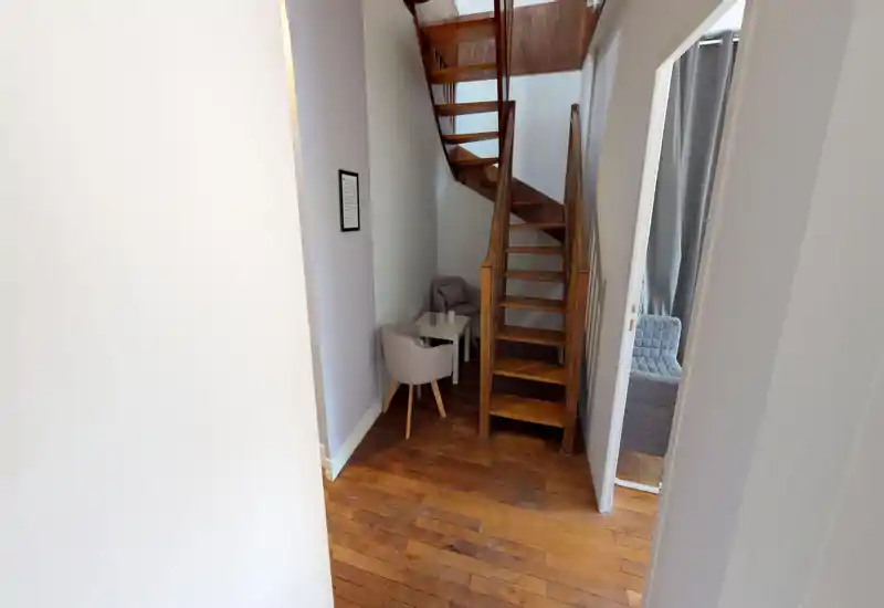 Compact entrance/landing with wooden stairs, a small seating nook and warm hardwood floors — well-lit and tidy, ideal as a cozy transitional space.
