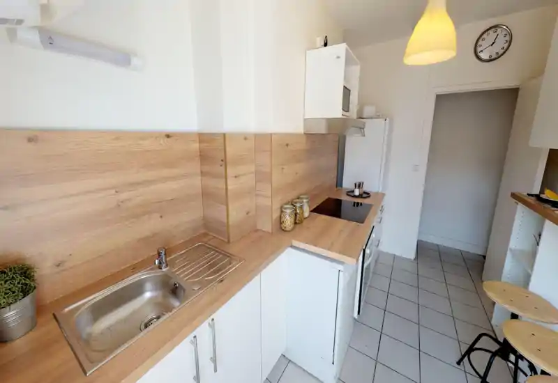 Cucina compatta e moderna con piano in legno, lavello in acciaio, piano cottura in vetroceramica e piccolo bancone — luminosa e ordinata, ideale per cucinare in modo efficiente.