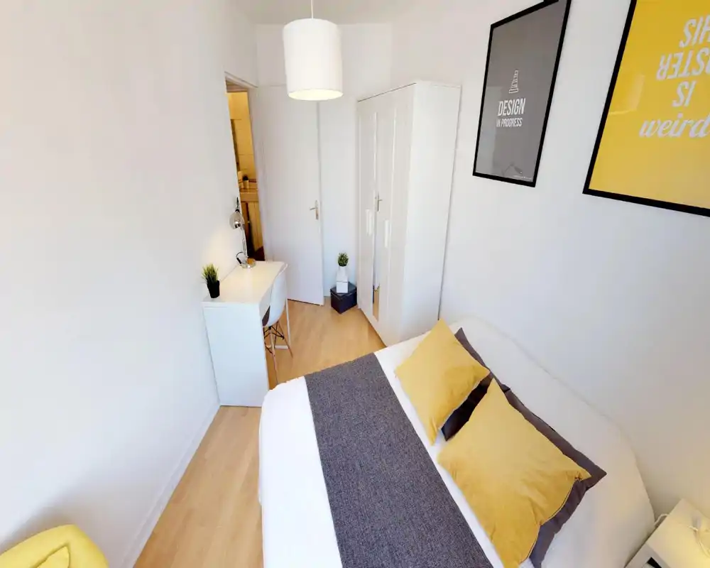 Bright, well-staged bedroom with a large bed dressed in white and yellow linens, a small desk and wardrobe—ideal for a single or couple seeking a cozy, contemporary room.