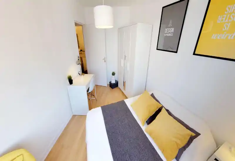 Bright, well-staged bedroom with a large bed dressed in white and yellow linens, a small desk and wardrobe—ideal for a single or couple seeking a cozy, contemporary room.