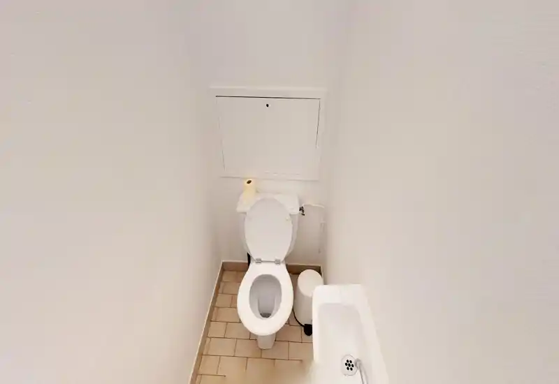 Small, well-lit WC with a standard toilet, a compact sink and tile floor — simple and clean facilities ideal for a guest restroom.