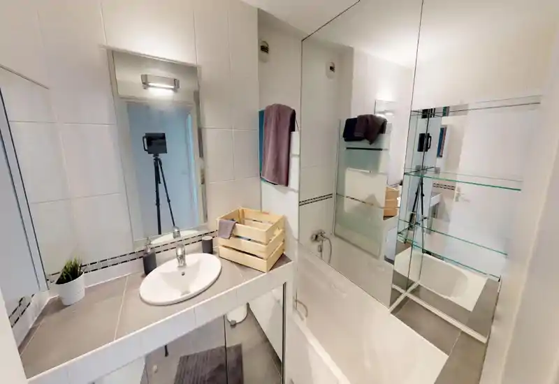 Bright, modern bathroom with a sink, bathtub and large mirror; neutral tiles and neat accessories create a clean, functional space.