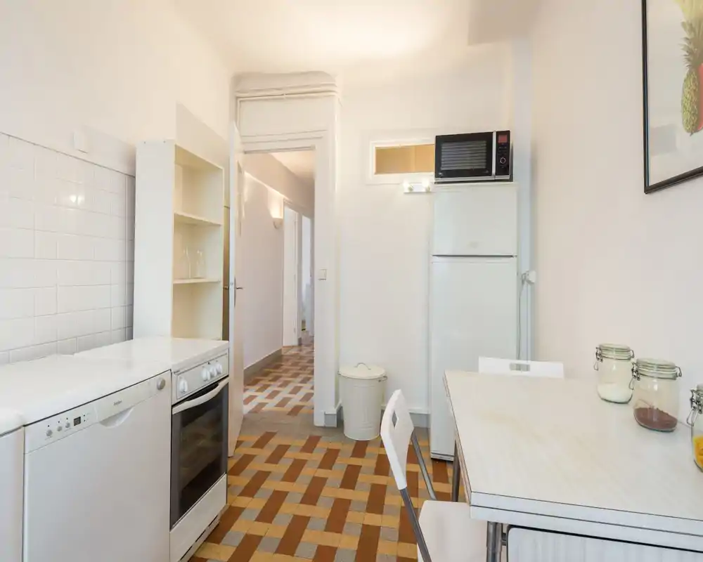 Cuisine compacte et lumineuse avec appareils blancs, réfrigérateur et four indépendants et petite table — propre et fonctionnelle.