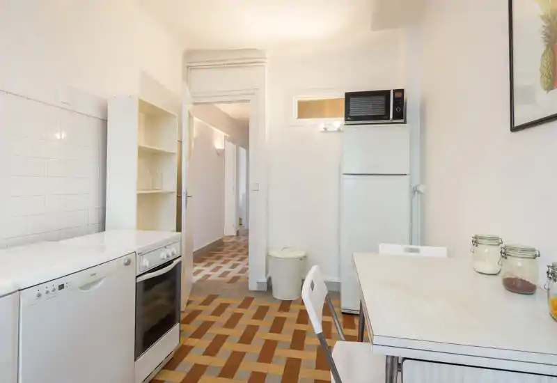 Bright compact kitchen with white appliances, a freestanding fridge and oven, and a small dining table — tidy and functional for short stays.